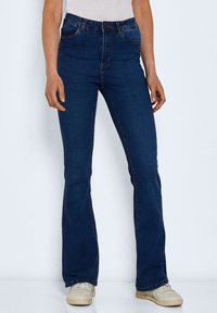 Tummansiniset, leveät farkut korkealla vyötäröllä, valmistettu denimestä. Ominaisuuksiin kuuluu viiden taskun malli ja napitus vyötäröllä.