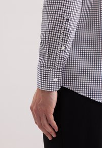 Biała i granatowa koszula w kratę z guzikami, z charakterystycznym kołnierzykiem i mankietami na dwa guziki, wykonana z gładkiego materiału i z dopasowanym krojem.