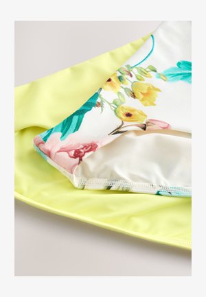 Kolorowa tkanina w kwiaty, złożona na jednolitym żółtym podkładzie, ukazująca żywe kwiaty na białym tle oraz gładką fakturę.