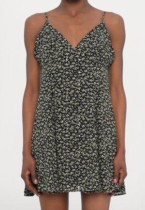 Czarna sukienka w kwiaty z dekoltem w serek, cienkimi ramiączkami i zwiewnym, rozkloszowanym krojem w kształcie litery A. Całość zdobią drobne zielone i białe wzory kwiatowe.
