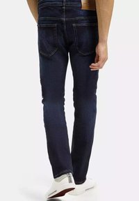 Ciemnoniebieskie dżinsy o dopasowanym kroju, pięć kieszeni, subtelne przeszycia i skórzana metka na tylnej części pasa.