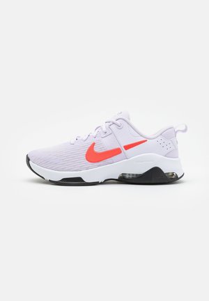 Baskets Nike violet clair avec semelle blanche, semelle extérieure noire, swoosh orange vif et amorti Air Zoom visible sous le talon.