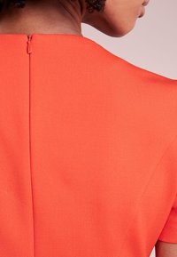 Haut orange ajusté en tissu lisse et texturé ; doté d'une fermeture éclair discrète au dos, au niveau de l'encolure.