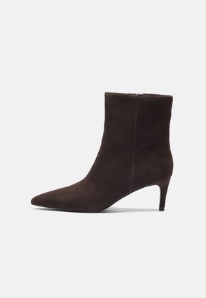 Brune semskede ankelstøvler med spidse tæer og 7,5 cm hæl, der har en glat tekstur og minimalistisk design. Lynlåslukning bagpå.