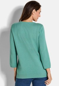 Ein mintgrüner Strickpullover mit einem strukturierten Muster und drei Viertel-Ärmeln. Er hat einen runden Halsausschnitt und einen gerippten Saum.