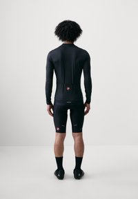 Tett svart langermet sykkeltopp og shorts med reflekterende detaljer og en logo-lapp. Glatt, elastisk stoff; stilrent, minimalistisk design.