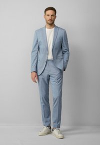 Hellblau gemusterter Anzug mit schlanker Passform, der ein einreihiges Blazer und passende Hose umfasst. Kombiniert mit einem weißen T-Shirt und Sneakers.