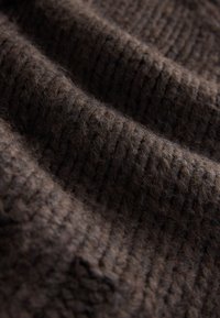 Tessuto marrone intrecciato con una texture rigata, che mostra fili morbidi e una superficie leggermente pelosa, indicando un materiale caldo e accogliente.