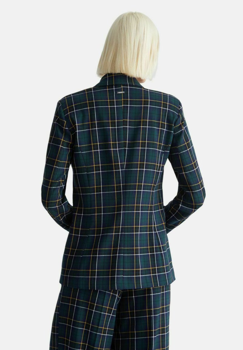 Blazer a quadri con una base verde scuro, dettagli gialli e bianchi. Schiena con doppia apertura e vestibilità slim. Il materiale appare composto e su misura.