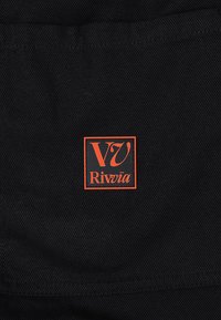 Schwarzer Stoff mit strukturierter Oberfläche und einem orangefarbenen quadratischen Logo, das "V7 Rivvia" in stilisierten Buchstaben zeigt.