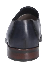 Donker marineblauwe leren schoenen met een gladde structuur, contrasterende bruine houten hak en een minimalistisch design, gezien vanuit de achterkant.