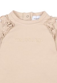 Sweatshirt beige avec des accents volants sur les épaules et le nom de la marque "TRUSSARDI" brodé dans un fil assorti. Fermeture à pression au niveau du cou.