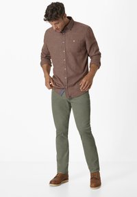 Brown patterned button-up shirt with rolled sleeves, paired with light olive green pants and brown lace-up shoes.
