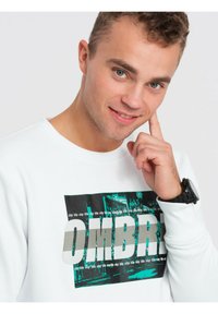 Biała bluza z grafiką w zielonym i szarym kolorze, z wyraźnie wyeksponowanym napisem "OMBRO". Miękka tkanina i swobodny fason.