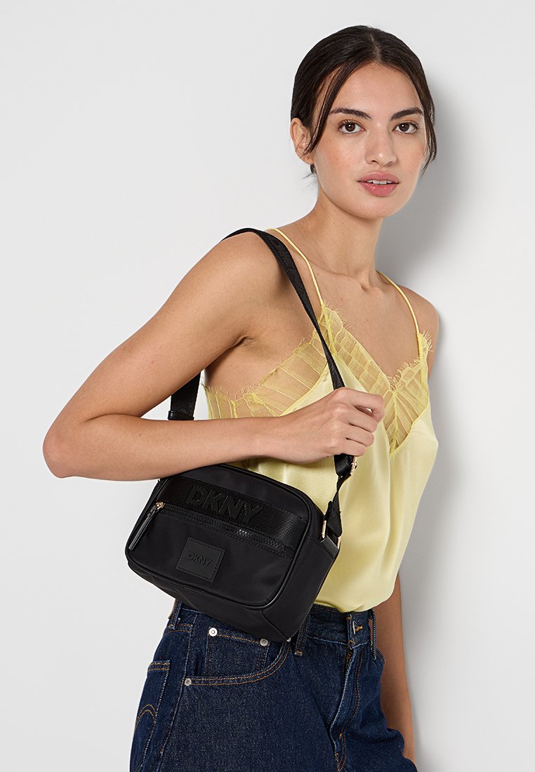 Bolso cruzado rectangular negro hecho de cuero suave con una correa texturizada de marca y un bolsillo frontal, con un cierre y acentos dorados.