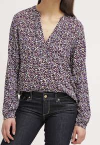 Blouse à manches longues et col en V avec imprimé floral violet, bleu et crème, coupe décontractée et petits boutons au col.