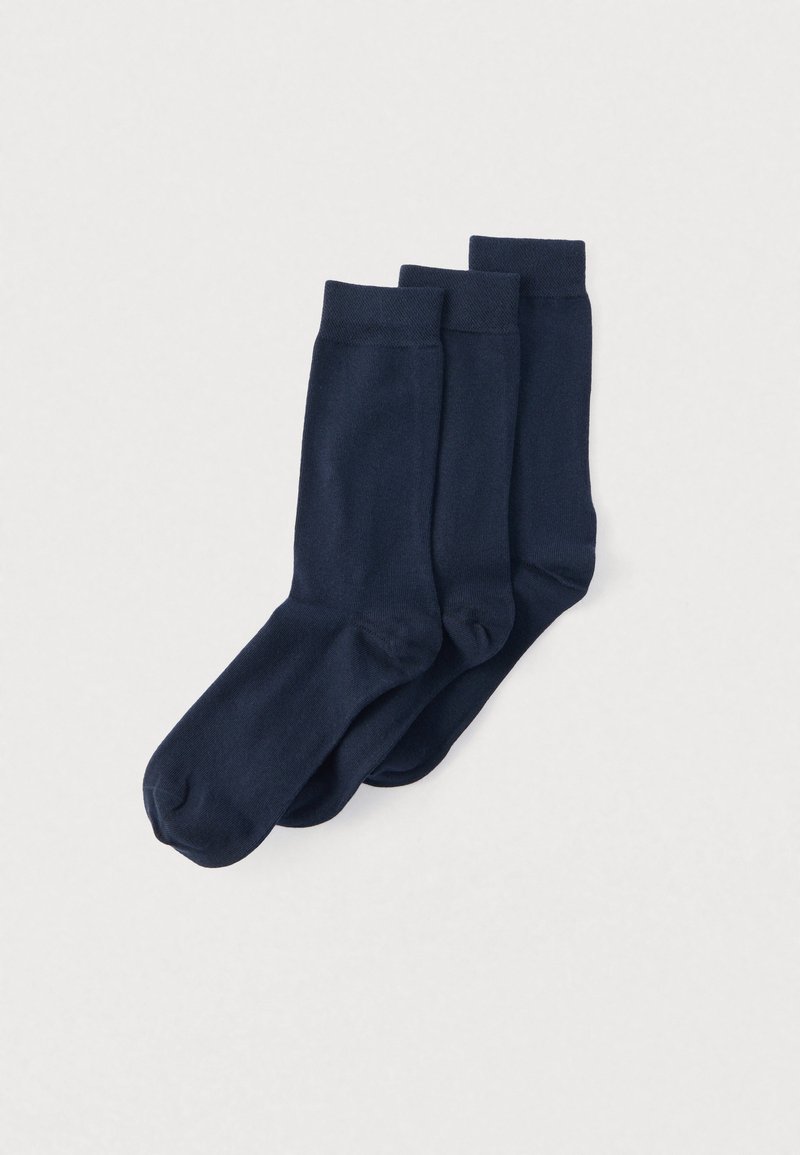 Trois paires de chaussettes unies bleu marine de longueur moyenne empilées proprement sur un fond gris clair.
