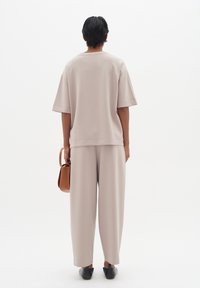 Light beige cohesive outfit comprising a relaxed-fit short-sleeve top and wide-leg pants, paired with a small brown handbag and black shoes.
