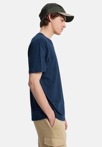 Marineblå bomulds T-shirt med korte ærmer, der har en klassisk pasform og en subtil tekstur. Sammen med beige cargobukser.