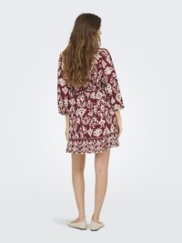 Abito bordeaux con motivo floreale bianco, presenta maniche a tre quarti, un orlo svasato e una cintura legata in vita. Tessuto con una texture morbida.