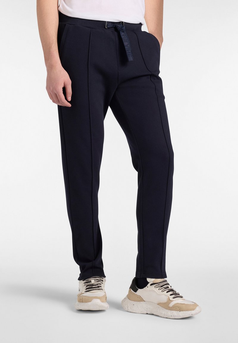 Mørkeblå bukser med tekstureret stof, tapered pasform og sidelommer. Har en justerbar talje og kontrastvæde. Matchet med sneakers.