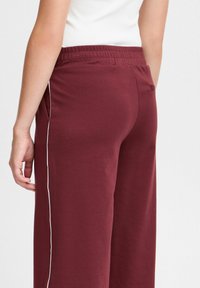 Mörkröda vida byxor med elastiskt midjeband, med en sidodetalj i vit piping och en bakficka. Mjuk material med en slät yta.