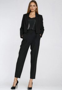 Czarna, dopasowana marynarka i spodnie o skrojonym fasonie. Góra ma czarną, cekinową fakturę. Szpilki dopełniają monochromatyczny look.