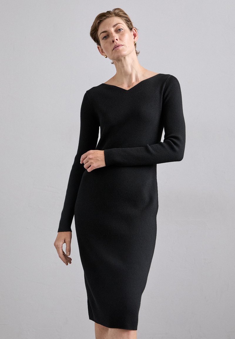 Black ribbed knit dress with long sleeves, V-neck, and a fitted silhouette. The texture is smooth and slightly stretchy.