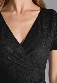 Robe noire à manches courtes, avec une texture en dentelle délicate et des motifs floraux complexes sur le tissu, design en V.