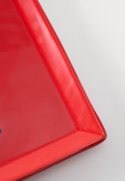 Κόκκινο κεραμικό πιάτο με γυαλιστερό φινίρισμα, τετράγωνο σχήμα και ελαφρώς ανυψωμένες άκρες, με διακριτική υφή και μονόχρωμο χρώμα.