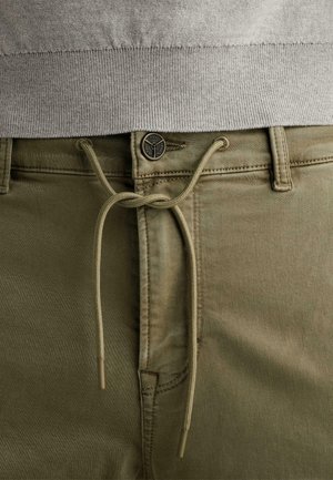 Nahaufnahme von khakifarbenen Hosen mit einem in eine Schleife gebundenen Kordelzug und einem Metallknopf, getragen unter einem grauen, gerippten Pulloressaum.