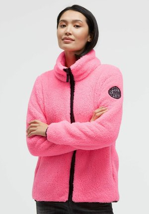 Fuzzy pink fleece jacket with a high collar and black zipper, featuring a circular logo on the left sleeve and elastic cuffs.