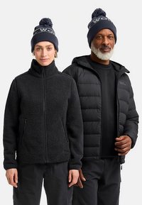 Schwarze Fleecejacke mit Frontreißverschluss und Taschen, kombiniert mit einer schwarzen Steppjacke, beide getragen mit gestrickten Mützen mit Bommel.