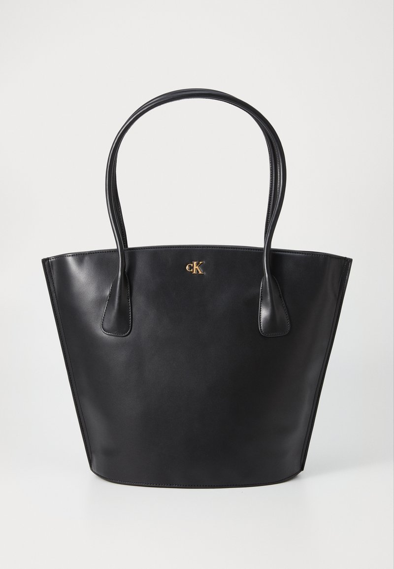 Sac fourre-tout en cuir noir avec deux poignées arrondies, texture lisse et un accent doré avec logo sur le devant. Conception à ouverture sur le dessus sans fermeture.