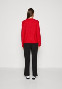 Pull en texture rouge, pantalon noir et baskets noir et blanc. Le pull a un col arrondi et une coupe décontractée, avec des manches longues.