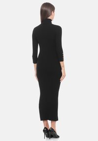 Abito midi nero a coste con collo alto, maniche a tre quarti e dettagli con bottoni dorati sulle maniche. Tessuto liscio e silhouette aderente.