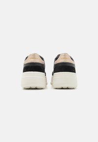 Sneaker in suede nero con suola platform color crema, caratterizzate da un accento in pelle beige sul tallone e logo in rilievo sul retro per un tocco moderno.