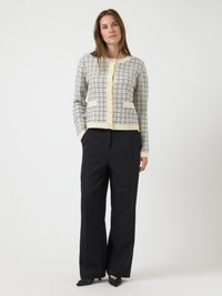 Πλεκτό κασκόλ με κρεμ και ναυτικό γεωμετρικό μοτίβο, διαθέτει κλείσιμο με κουμπί, δύο μπροστινές τσέπες και rib λαιμόκοψη. Συνδυάζεται με μαύρο παντελόνι.