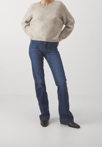 Maglione beige lavorato a maglia con scollo tondo, abbinato a jeans blu scuro a zampa d'elefante e stivali neri con punta. Design semplice con dettagli minimi.