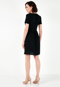 Abito nero a maniche corte con corpetto aderente e gonna svasata. Tessuto morbido, lunghezza al ginocchio, abbinato a scarpe con tacco beige.