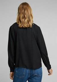 Sort langærmet skjorte lavet af blødt stof. Har en afslappet pasform med en rundet kant og plisseret ryg for ekstra tekstur og detaljer.