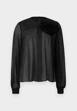 Blusa nera con maniche lunghe in tessuto trasparente, caratterizzata da pieghe frontali e un fiore in tessuto a strati come dettaglio sulla spalla sinistra. Chiusura con bottone al collo.