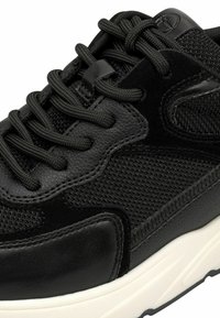 Schwarzer Sneaker aus einer Kombination von strukturiertem Mesh und glattem Leder, runde Form, kontrastierende weiße Gummisohle und flache Schnürsenkel.