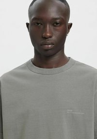 Hall riidest T-särk ümarkaelusega, lühikeste varrukatega ja peene brändinguga vasakul rinnal. Pehme tekstuur, lõdvestunud istuvus.