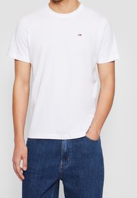 Vit bomulls t-shirt med korta ärmar och rundad hals. Har en liten röd, vit och blå logotyp på övre vänstra bröstet.