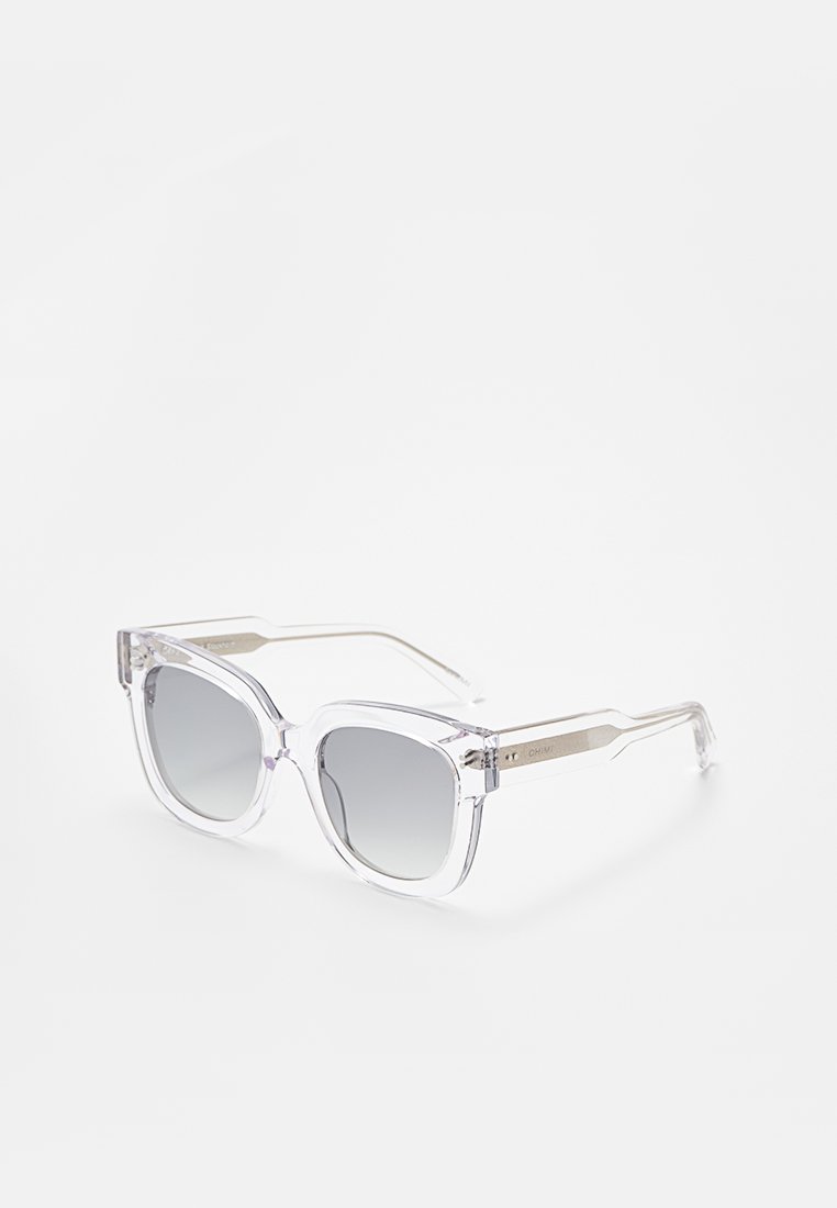 Gafas de sol de plástico transparente con lentes de degradado gris. Montura cuadrada con bordes angulares y acentos en tono plateado en las patillas.