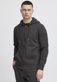 Grijze zip-up hoodie gemaakt van zachte stof, met een capuchon met trekkoord, voorzakken en geribbelde boorden. Soepele textuur met een casual pasvorm.