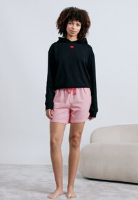 Fekete, cropped kapucnis pulcsi, kis piros címkével, rózsaszín, pöttyös sorttal párosítva, amely rugalmas derékkal és zsinórral rendelkezik.