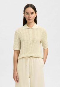 Polo shirt couleur crème avec un design texturé en tricot, à manches courtes et patte de boutonnage. Assorti à un pantalon décontracté de coupe ample.