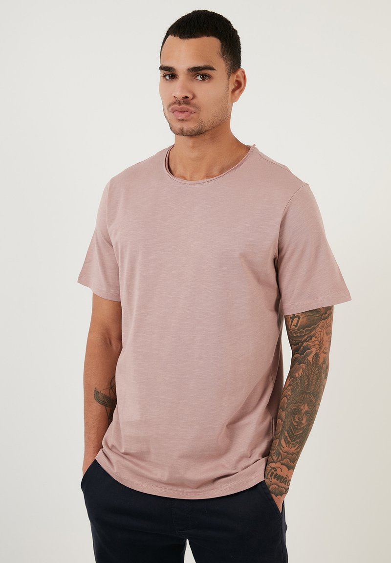 Tricou scurt cu mânecă scurtă, de culoare roz deschis, cu guler rotund, textură moale, croi lejer, cu detalii de cusătură subtile și un design minimalist.
